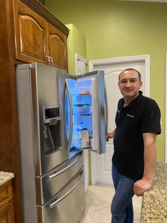 Refrigerator repair technician inspecting French door fridge in Tampa home kitchen
