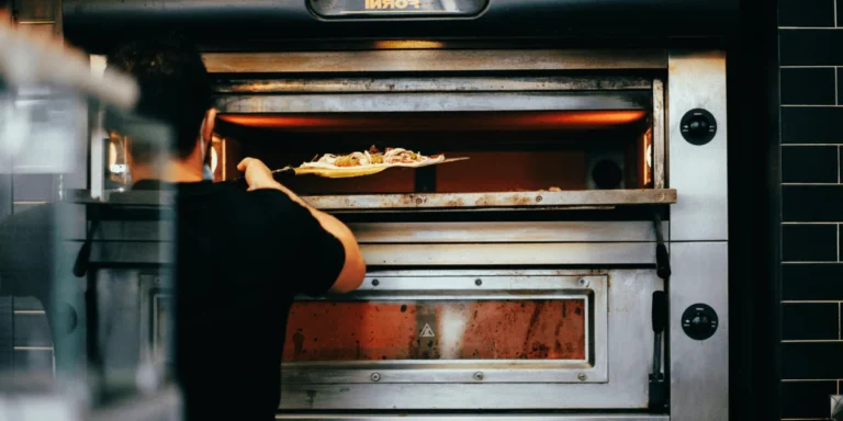 Cook loading pizza into hot commercial deck oven in busy Tampa kitchen